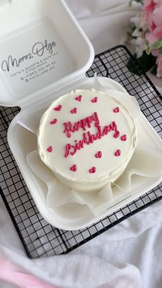 a white cake with pink hearts on it sitting in a plastic container next to flowers