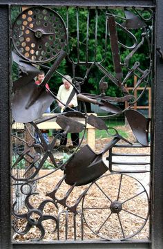 an iron gate with various metal objects on it's sides and people in the background