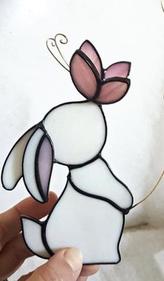 a hand holding a stained glass rabbit ornament with pink and white accents on it