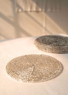 two round silver coasters sitting on top of a white table cloth covered in sequins