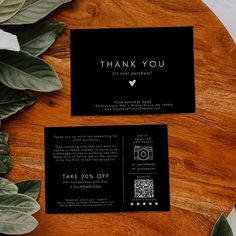 a black and white thank you card sitting on top of a wooden table next to green leaves