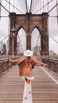 a woman walking across a bridge with her arms spread out in front of the camera