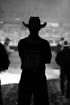 the back of a cowboy standing in front of a crowd at a sporting event with people watching