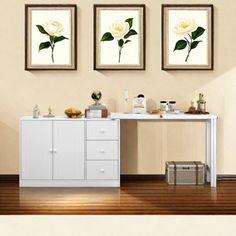 three framed pictures hang on the wall above a white cabinet with drawers and two vases