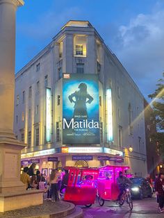 people are walking and riding bikes in front of a building with a sign that reads matilda