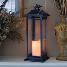 a lit candle sitting on top of a mantle next to a vase with dried flowers