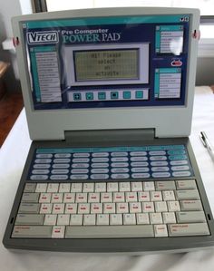 an old laptop computer sitting on top of a white tablecloth covered table with a pen and paper