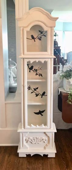 a white china cabinet with birds painted on the front and bottom shelves, sitting in a living room