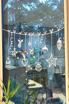 a window decorated with christmas decorations and ornaments hanging from it's side, next to a potted plant