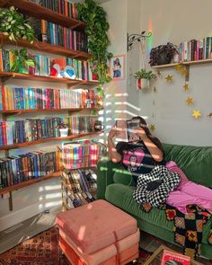 a woman sitting on top of a green couch in front of a bookshelf