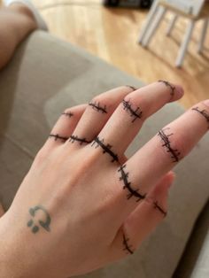 a person's hand with barbed wire tattoos on their thumb and ring, sitting in front of a couch