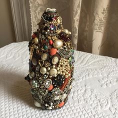 a vase with lots of different types of jewelry on it sitting on a bed next to a window