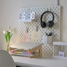 a white desk with headphones on it next to a wall mounted clock and notepads