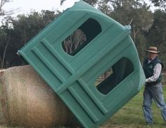 a man standing next to a large hay bale in the middle of a field