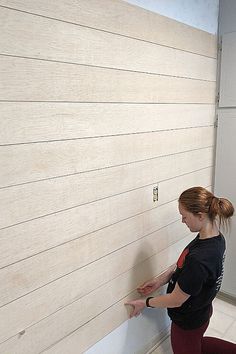 a woman standing in front of a white wall with wood planks on the walls