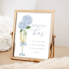 a blue hydrangea flower in a champagne glass is displayed on a gold frame