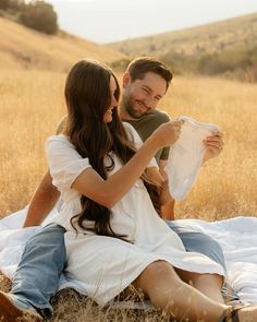 a man and woman sitting on top of a blanket in the middle of a field