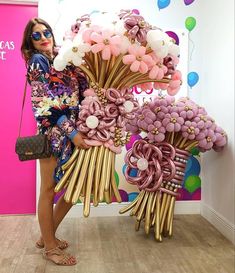 a woman standing next to a large bouquet of flowers in front of a pink wall