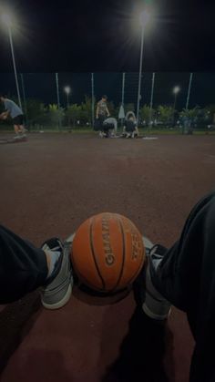 an orange basketball sitting on the ground in front of some people with their feet up