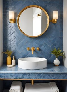 a bathroom with blue tile and gold accents on the wall, round mirror above the sink