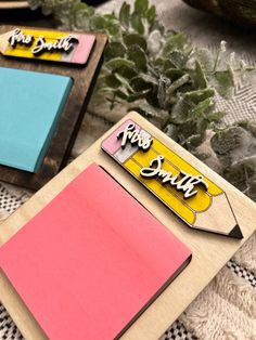 three different colored sticky notes sitting on top of a wooden board next to some succulents