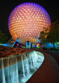 the spaceship ball is lit up at night in front of a water fountain and building