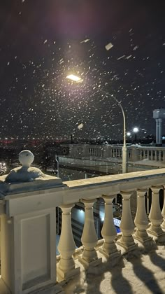 snow falling in the night sky over a balcony with white railings and lights on