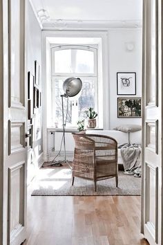 an open door leading to a living room with white walls and wood floors, along with a wicker chair