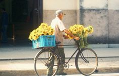 an old man is riding his bike with sunflowers in the basket on the street