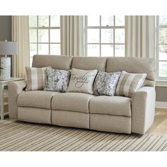 a beige couch with pillows on it in front of two windows and a striped rug