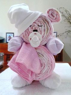 a teddy bear wrapped in blankets and wearing a hat is sitting on a bed with a pink blanket