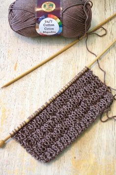 two skeins of yarn sitting next to each other on a wooden table with knitting needles