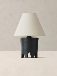 a black table lamp sitting on top of a white floor next to a gray wall