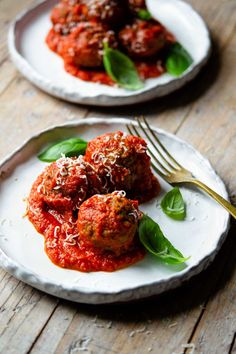 two white plates topped with meatballs covered in marinara sauce and sprinkled with parmesan cheese