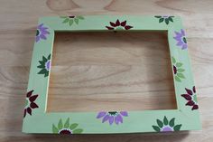 a green frame with flowers painted on it sitting on top of a wooden table next to a piece of wood