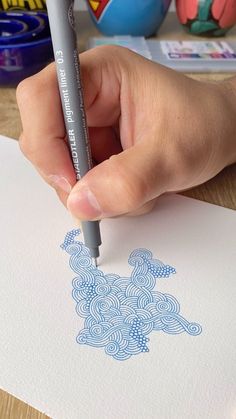 a hand holding a marker and drawing on paper with blue ink in front of it