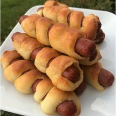 several hot dogs wrapped in bread on a white platter with grass in the background