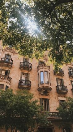 an old building with balconies and trees in the foreground, looking up at the sky