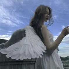 a woman dressed in white holding a cell phone with angel wings on her shoulders and arms