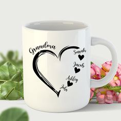 a white coffee mug with the words grandma and two hearts on it next to pink flowers