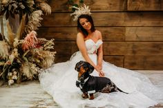 a woman in a wedding dress kneeling next to a dachshund wearing a tulle