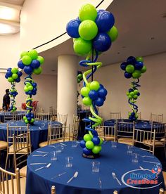 blue and green balloons are hanging from the ceiling at a banquet table set up for an event