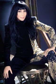 a woman sitting on top of a chair wearing black and gold clothes with long hair