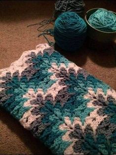 a blue and white crocheted blanket sitting on the floor next to some yarn