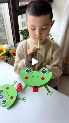 a young boy holding a pencil in his mouth and looking at two green frog puppets