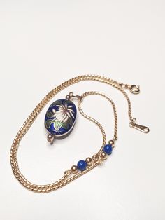 Avon necklace showcases a gold tone chain. The pendent  itself boasts s striking  blue background with a white flower at its center, surrounded with green leaves. The over all effect is one of simple beauty. Simple Beauty, Long Beach, White Flower, Blue Background, Blue Backgrounds, Green Leaves, White Flowers, Shopping List, Jewelry Necklace Pendant