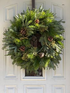 a wreath hanging on the front door of a house with pine cones and evergreen leaves