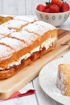 a piece of cake sitting on top of a wooden cutting board next to a bowl of strawberries