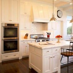 a kitchen with white cabinets and an island in the middle is lit by two pendant lights