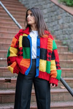 a woman standing in front of some stairs wearing a colorful sweater and black pants with buttons